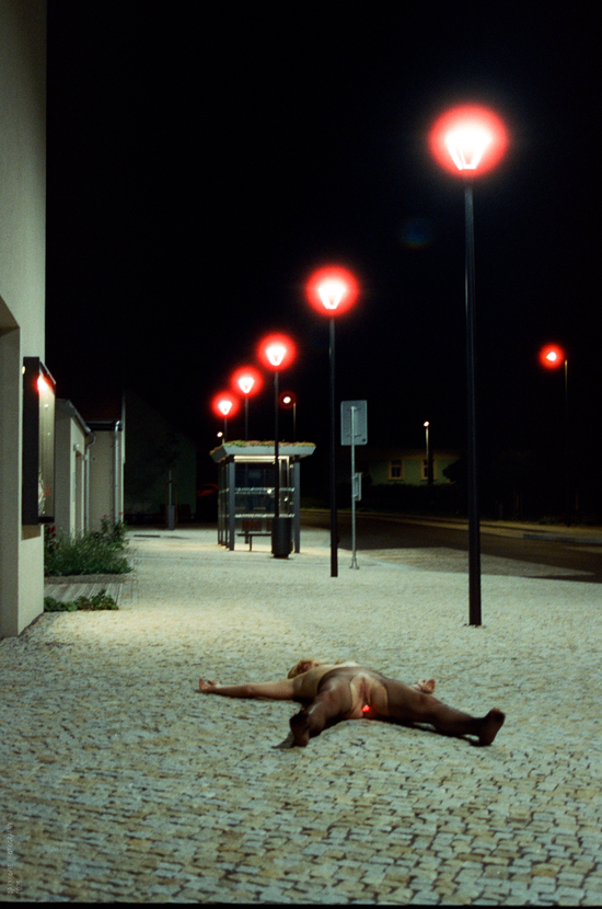Nahá dívka se svítcím análním kolíkem leží na noční ulici, foceno na Cinestill 800T.